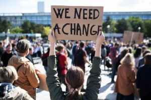 A woman holds up a sign reading “we need a change” at a political advocacy protest.