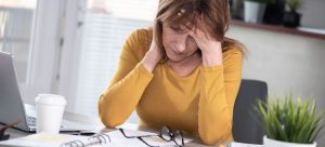 A case manager with a hand on her forehead as she looks down at her desk and workspace